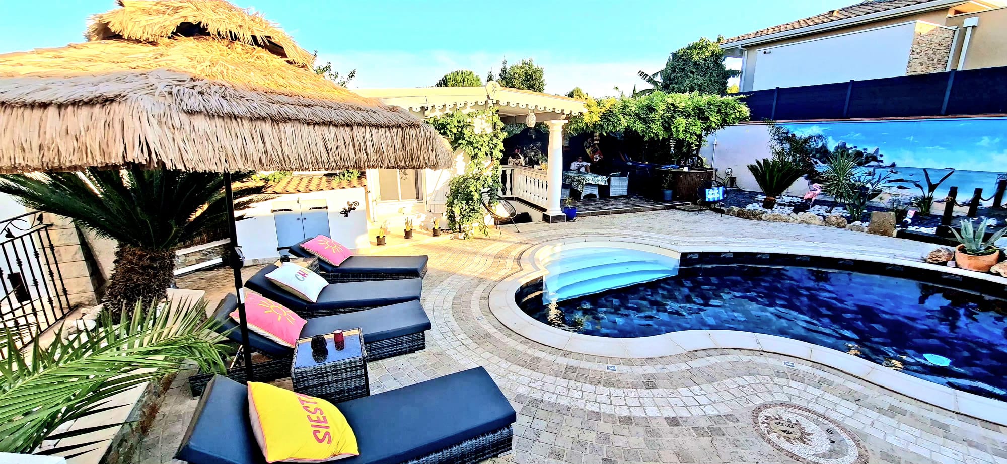 Piscine partagée avec parasol de paille et transats