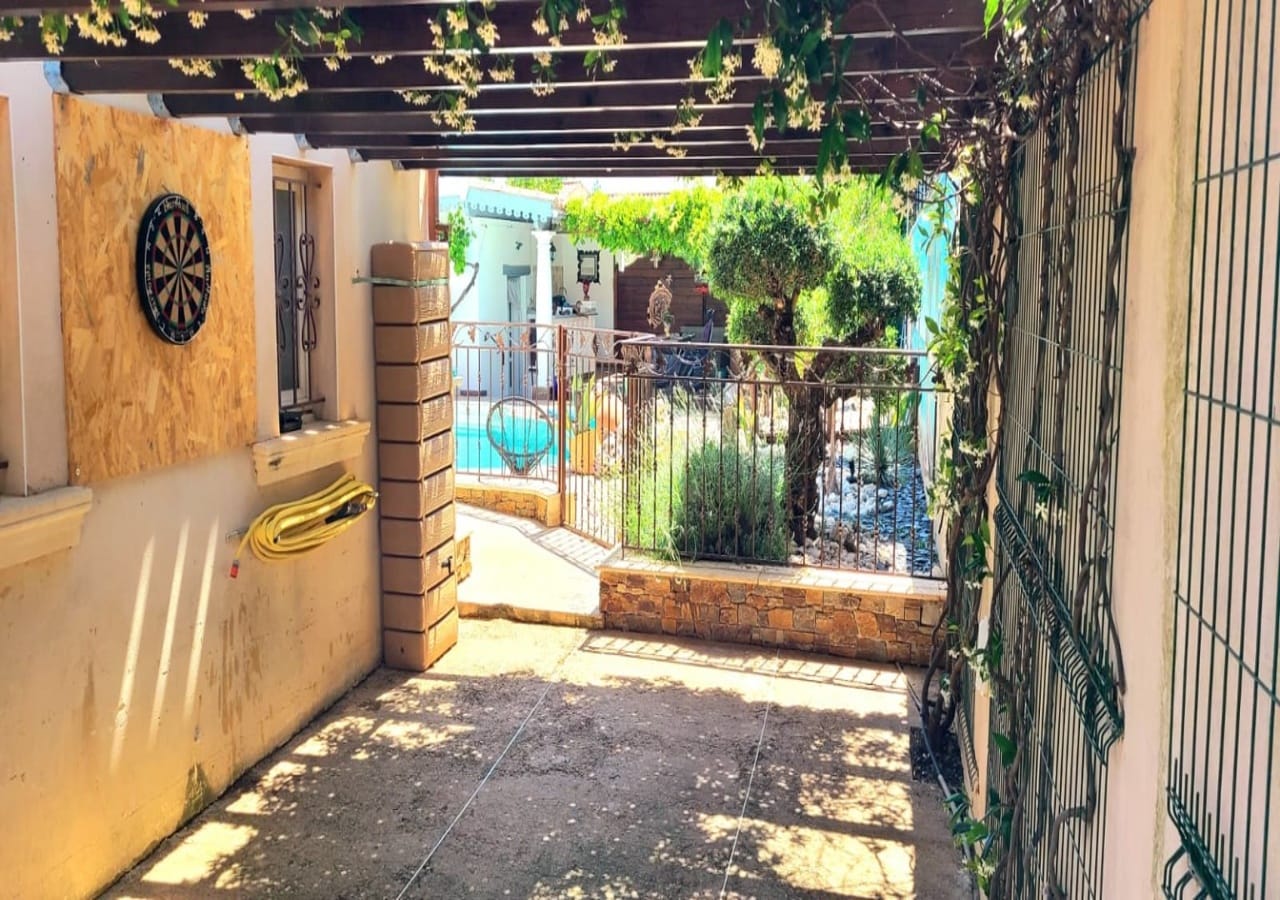 Passage sous pergola avec jeu de fléchettes, vue sur la piscine